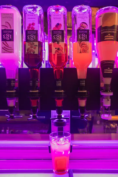 Dosierer der Cocktailmaschine füllen einen Cocktail ab, Flaschen kopfüber im Neonlicht